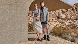 Two models stand in neutral-coloured luxury clothes in a desert landscape.